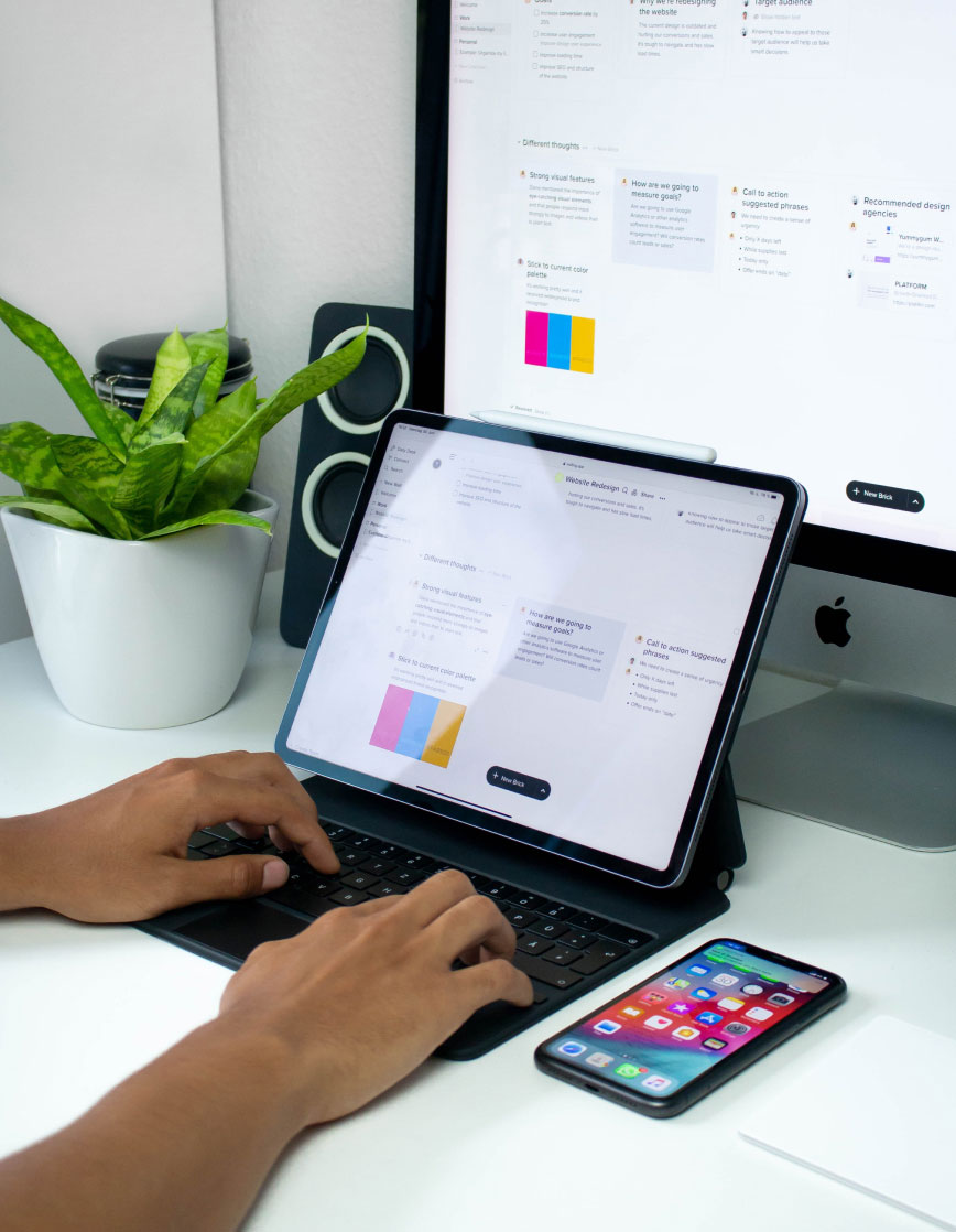 info-6 "Person working on tablet with keyboard in modern workspace, displaying UI/UX design tools, smartphone, desktop screen nearby."